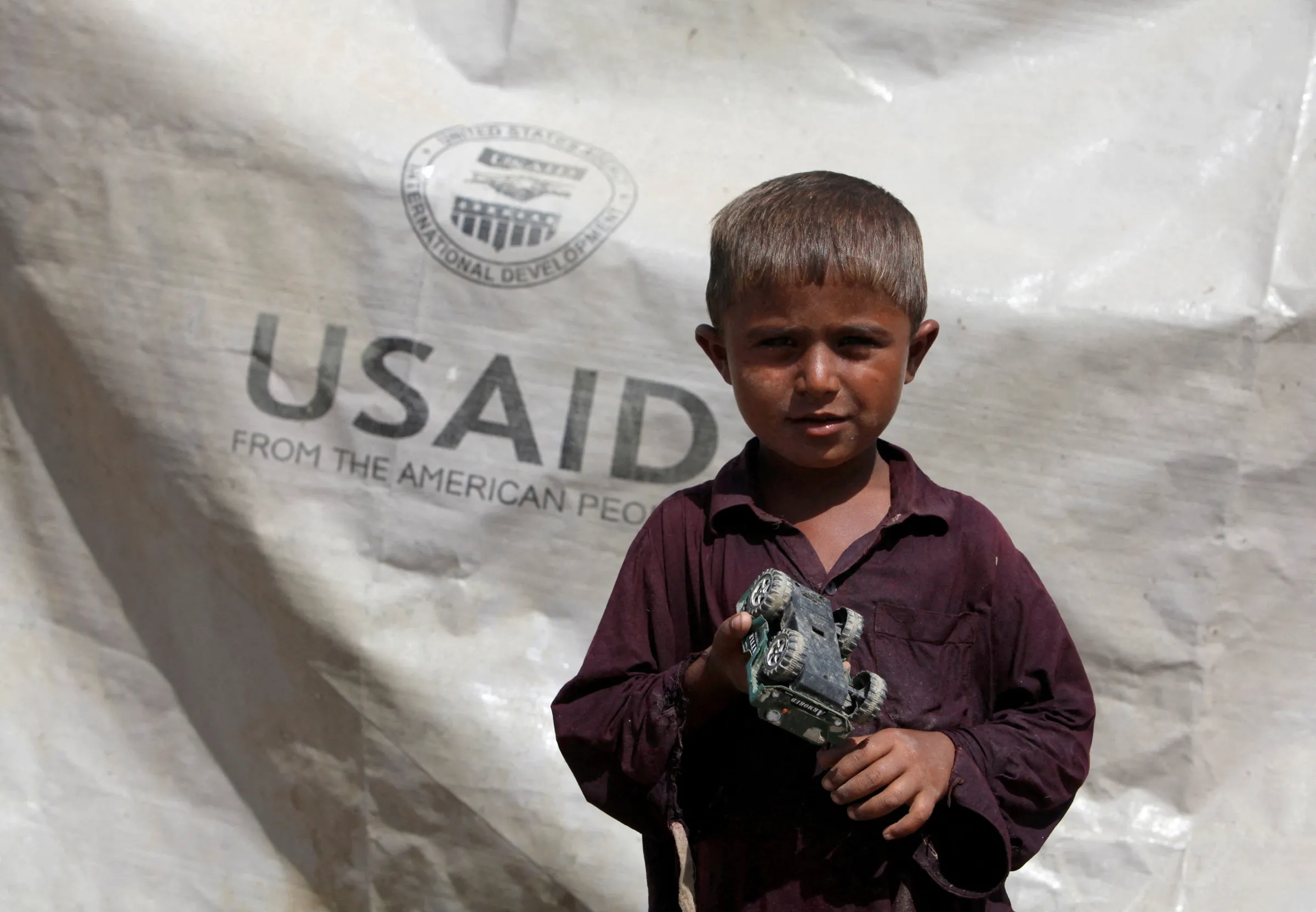 A boy who has been displaced by flooding, holds his toy jeep outside his family tent with the weather sheet donated by USAID in Pakistan's Sindh province October 5, 2010. REUTERS/Akhtar Soomro